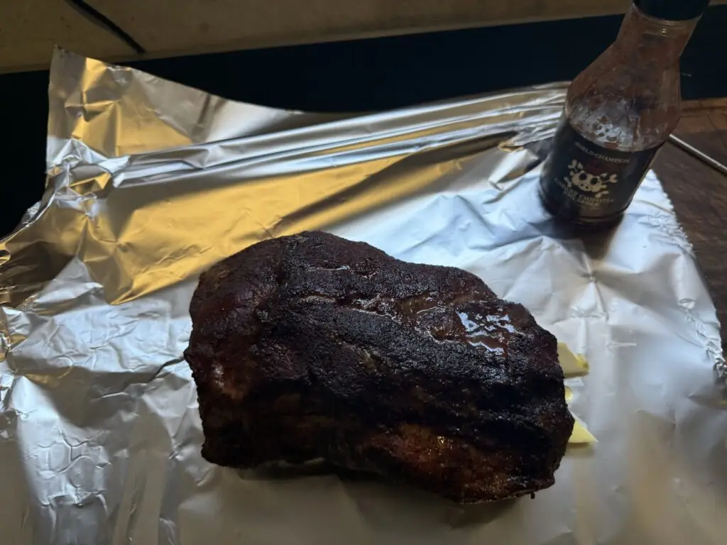 Svinjski vrat na aluminijskoj foliji s maslacem, pored boce Cherry Chipotle umaka